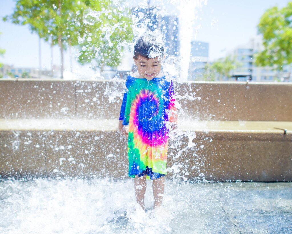 petit garon qui se rafraichit sous un jet d'eau dans la ville
