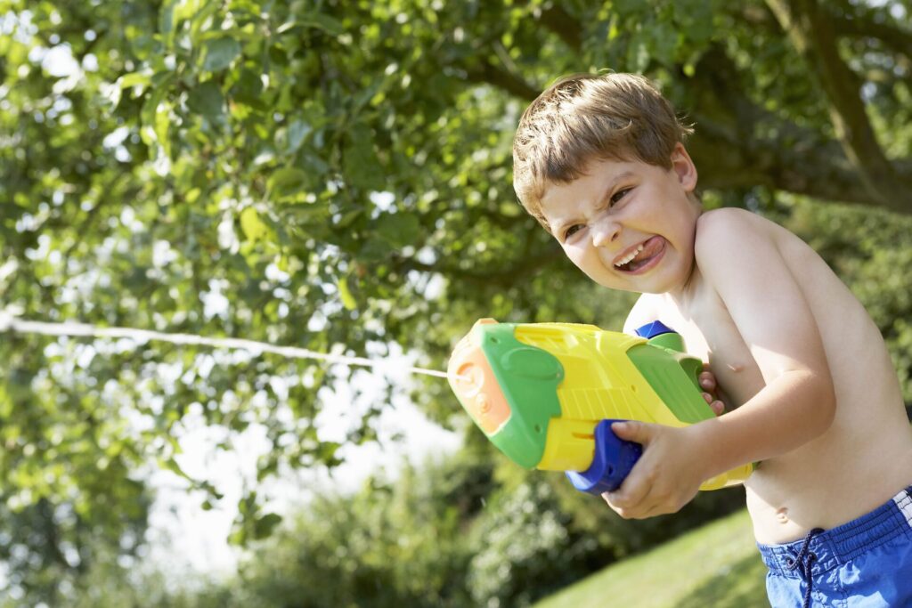petit garçon qui joue avec un pistolet à eau  dans un jardin